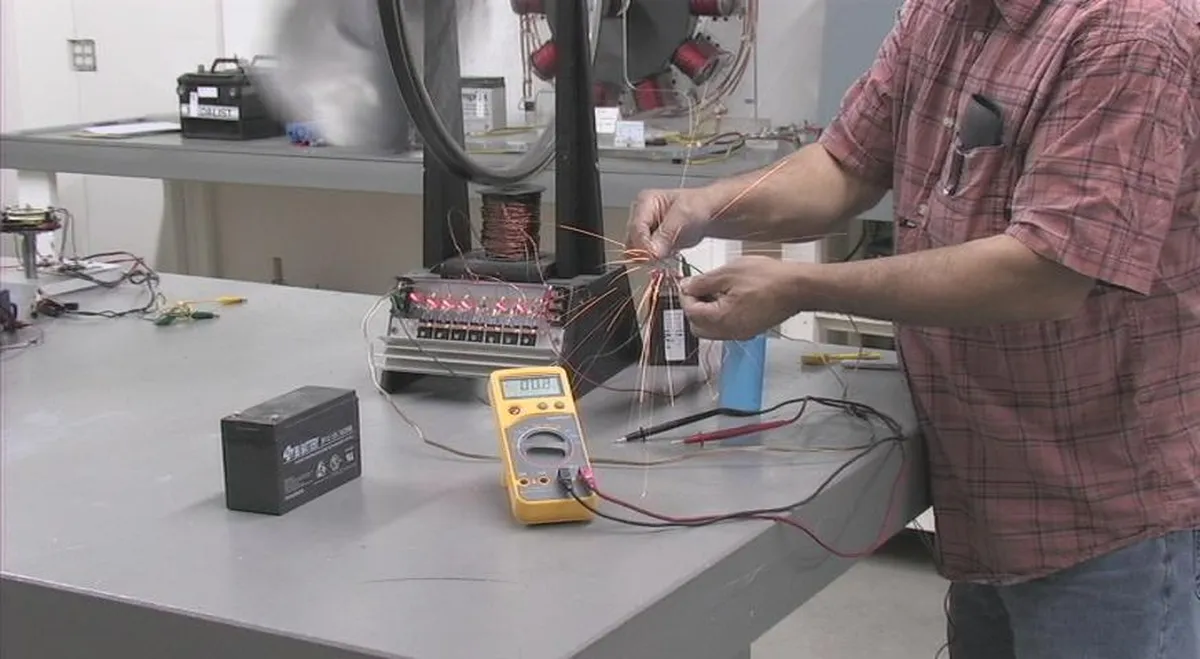 An electrician troubleshooting electrical circuits with a multimeter and battery on a workbench